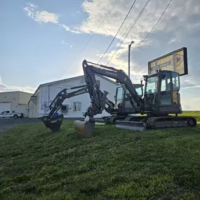 Two Volvo compact excavators parked on grass in front of the building