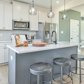 Kitchen with white cabinets, stainless steel appliances and gray island with 3 bar stools in DRB Homes Stonebridge Townhomes at Charles Pointe
