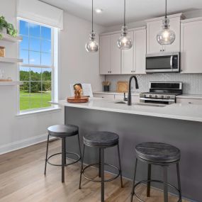 Kitchen with white cabinets, stainless steel appliances, island with gray cabinetry, and three barstools in DRB Homes Legacy community