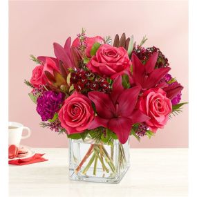 Radiant jewel tones set the tone for a romantic Valentine’s Day. Our eye-catching arrangement mixes classic roses and lilies with unique Leucadendron and dianthus. Gathered in a chic cube vase with lush touches of greenery, it’s a sweet and stylish expression of love.