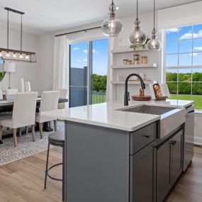 Kitchen island with gray cabinetry overlooking a dining room with long chandelier, a window and sliding glass door in DRB Homes Rolling Hills