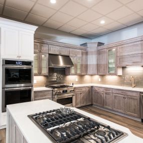 Kitchen showroom with a while kitchen island, stovetop, and stainless steel appliances