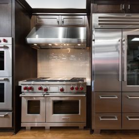 Stainless steel wall ovens, range, and refrigerator on display with dark wooden cabinets