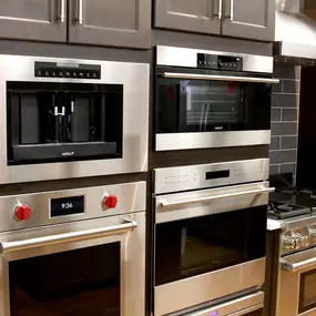 Stainless steel built-in wall ovens on display with dark wooden cabinets and a range on the side