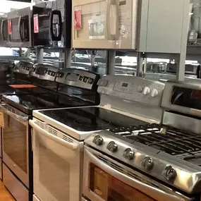 multiple kitchen ranges lined up on display with microwaves on display above them and wooden floors