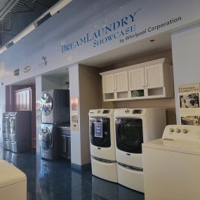 Laundry appliance showroom with white washing machines on display and dark flooring