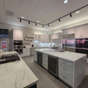 Kitchen appliance showroom with a gray kitchen island on display surrounded by white cabinets and stainless steel appliances