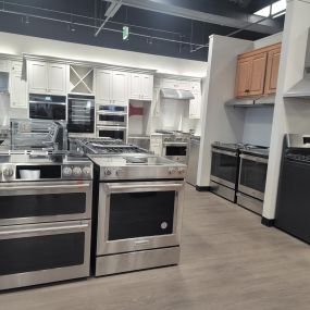Kitchen appliance show room with multiple stainless steel kitchen ranges and white cabinets in the back