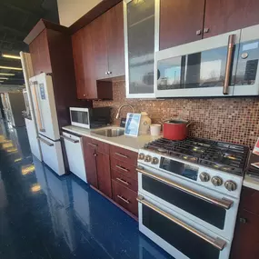 kitchen appliance display with wooden cabinetry, red and brown tile backsplash, and white appliances