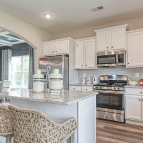Kitchen with white cabinets, stainless steel appliances and island in DRB Homes The Preserve community