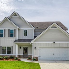 Two story home with tan siding and partial brick front with two car garage in DRB Homes The Preserve community