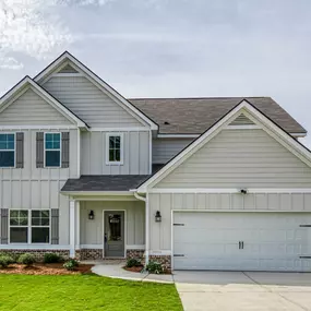 Two story home with tan siding and partial brick front with two car garage in DRB Homes The Preserve community