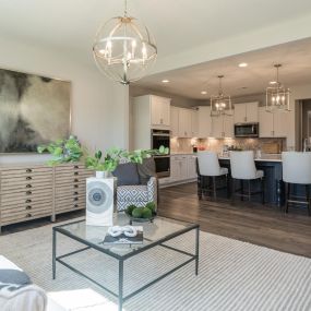 Family room with sitting area and gourmet kitchen with white cabinets and black island with 4 bar stools at DRB Homes Brighton Glen