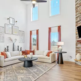 Family room with cathedral ceiling, couch and chair seating area and stone fireplace at DRB Homes The Grange community