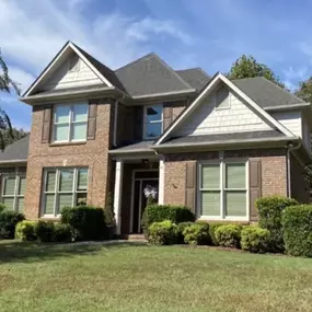 Brown brick home with white accents featuring a black asphalt shingle roof