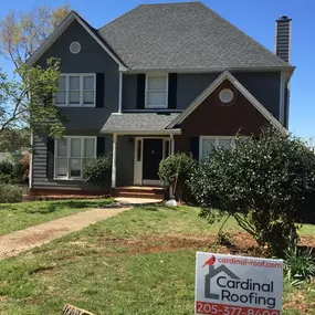 Gray-colored home featuring a Cardinal Roofing sign in the front yard