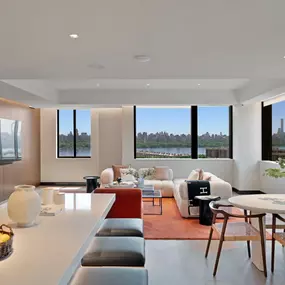 A dining room near a kitchen breakfast bar leads to a living room with large windows providing views of the Hudson River and Manhattan.