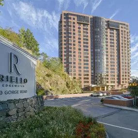 Exterior view of Riello Edgewater's property sign in front of the high-rise apartment building with trees.