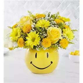 The best way to send along a little sunshine? You’re looking at it. Our new bouquet is filled with feel-good yellow blooms. We’ve gathered them into our keepsake smiley face container, bringing just the right amount of brightness to make their day better. Perfect for celebration-worthy moments and everyday sentiments! All-around arrangement with yellow roses, daisy poms, button poms, lavender carnations, purple dianthus and statice; accented with assorted greenery Artistically designed in our ce