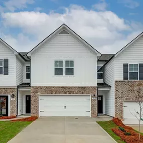 Row of 3 townhomes with 2-car garages with brown brick and white siding at DRB Homes The Borough at Wyndham South