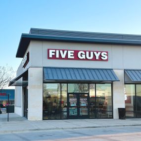 Exterior photograph of the entrance to the Five Guys restaurant at 6451 East NW Highway in Dallas, Texas.