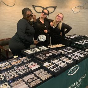 Michigan Eye Institute Employees standing behind a pop-up table displaying different styles of glasses and lenses.