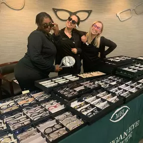 Michigan Eye Institute Employees standing behind a pop-up table displaying different styles of glasses and lenses.