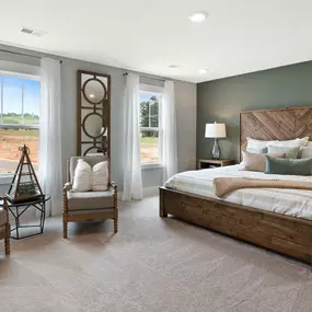 Owners' suite with recessed lighting, tan carpet, green walls and king size bed with two windows and seating area in DRB Homes Anderson Grant