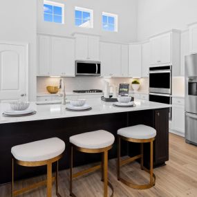 Kitchen with white cabinets, 3 windows above cabinets and stainless steel appliances. Large black kitchen island with 3 bar stools in the DRB Homes Deerfield Preserve community