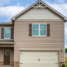 Two story single family home with tan siding and two car garage in the DRB Homes Towne Center community