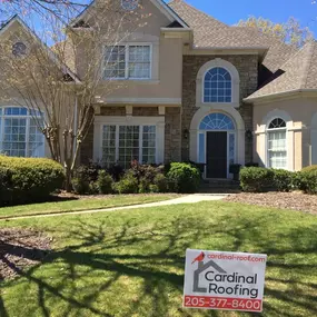 Tan luxury-style home showcasing a Cardinal Roofing sign in the front yard