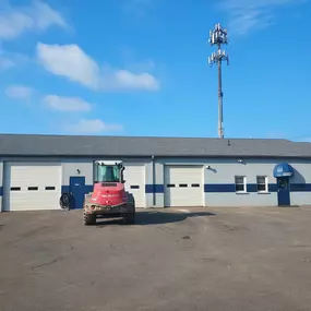 Rear view of the building with multiple service bay doors and a single Takeuchi loader parked on the lot