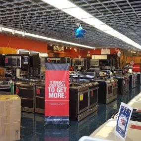 Home appliance showroom with various appliances on display and a red and black banner