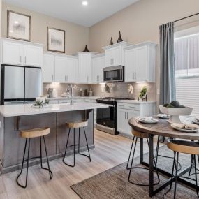 Kitchen with white cabinets and gray island with stainless steel appliances and dining area at DRB Homes Camden Cottages