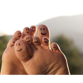 Bottom view of a pair of feet with smiley faces drawn on each toe with sky and trees in background