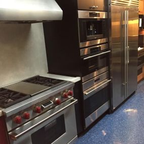 kitchen showroom with blue flooring and a stainless steel range, hood, ovens, and refrigerator on display