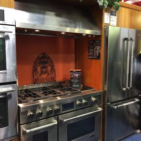 kitchen display with a stainless steel range, stainless steel refrigerator, hood, and orange backsplash