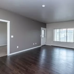 A large empty room with wood flooring and a window with blinds.