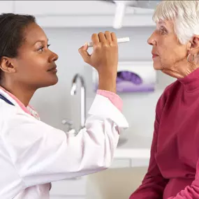 Optometrist using a penlight on a senior patient