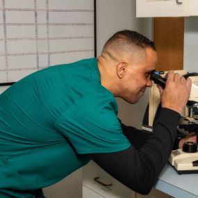 A veterinary technician examines a sample using a microscope in our on-site diagnostic laboratory.