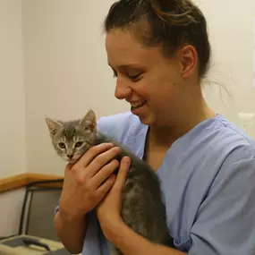 A veterinary technician is all smiles as she cozies up to a new kitten patient.