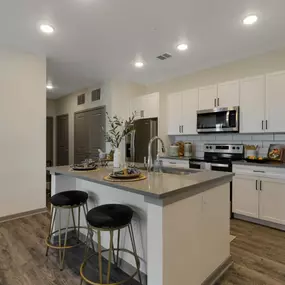 A kitchen with white cabinets and a large island with two stools