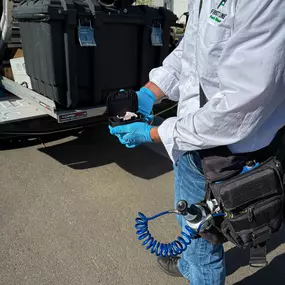 A First Line Pest Defense technician holding a pest control bait station, ready for deployment.