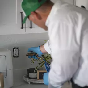 A First Line Pest Defense technician applying professional pest treatment indoors near a wall outlet.