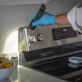 A First Line Pest Defense technician using a flashlight to inspect behind a kitchen stovetop for pests.