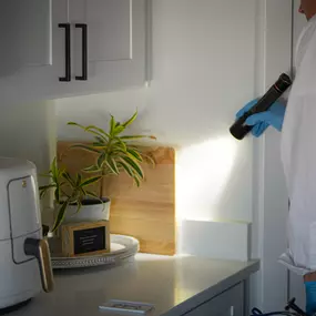 A First Line Pest Defense technician carefully inspecting a kitchen corner with a flashlight during a professional pest inspection.