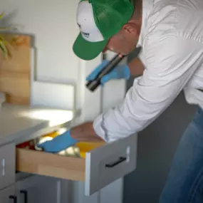 A First Line Pest Defense technician inspecting the inside of a kitchen drawer with a flashlight for pests.