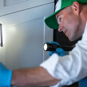 A First Line Pest Defense technician using a flashlight to inspect inside a kitchen cabinet for pests.