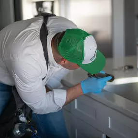 A First Line Pest Defense technician inspecting around a kitchen sink and faucet with a flashlight for pests.