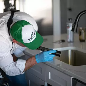 A First Line Pest Defense technician inspecting the edge of a kitchen counter near a sink with a flashlight for pest signs.